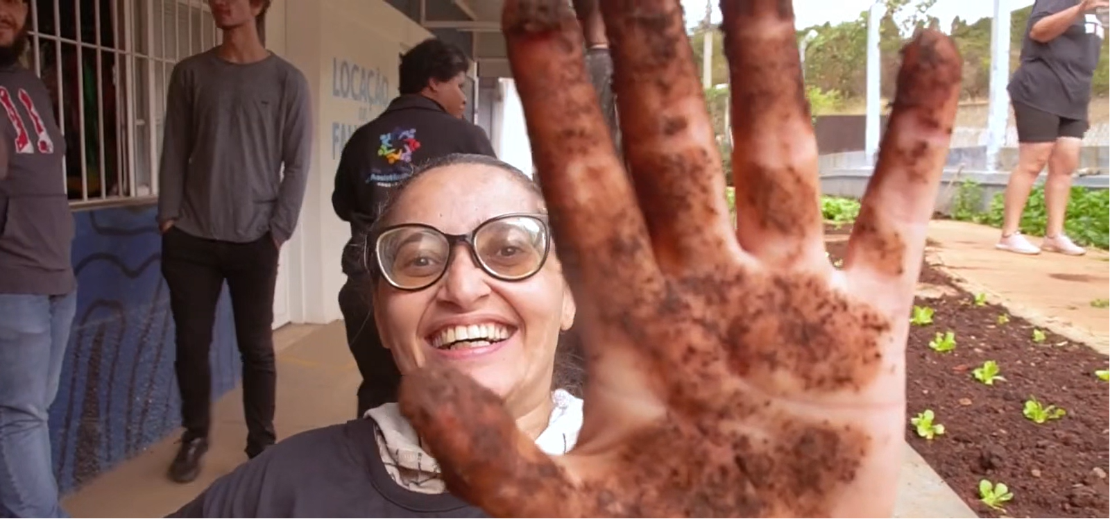 Educadora sorrindo com as mãos na terra durante atividade na horta